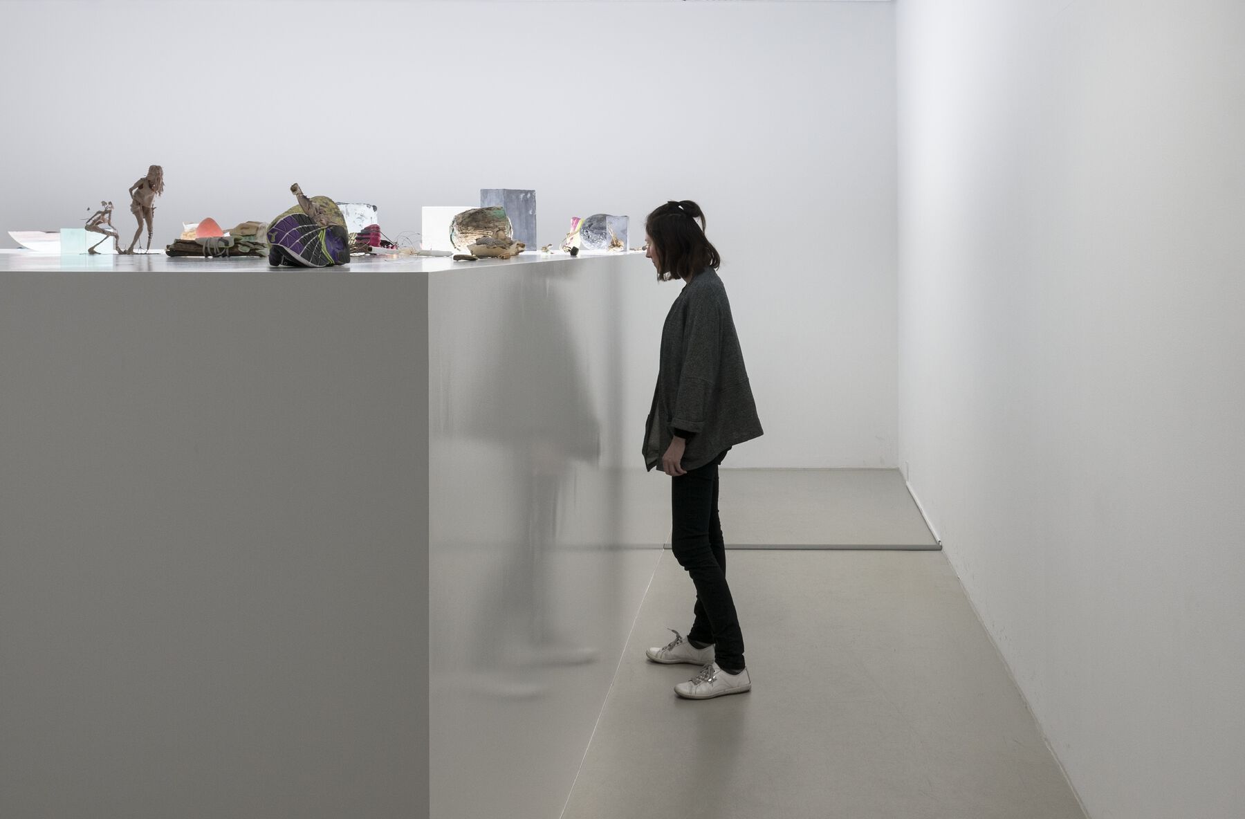 Person closely inspects object from large installation of sculptures on a plinth raised to eye-level