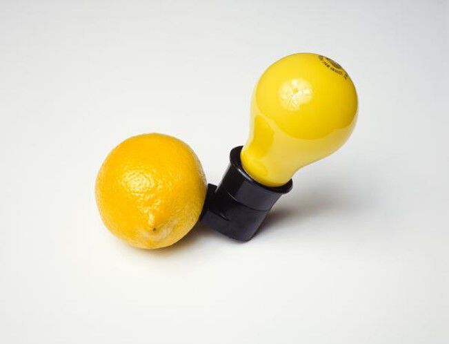 A lemon with a socket being stuck to it from the right side connecting it to a yellow light bulb