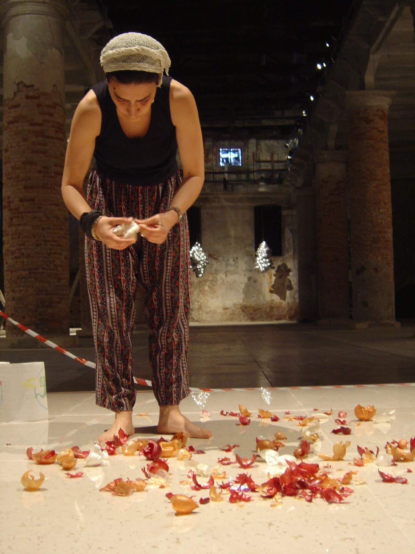 Artist standing barefoot on roped-off section in a dark room, placing torn onion peels on well-lit slab