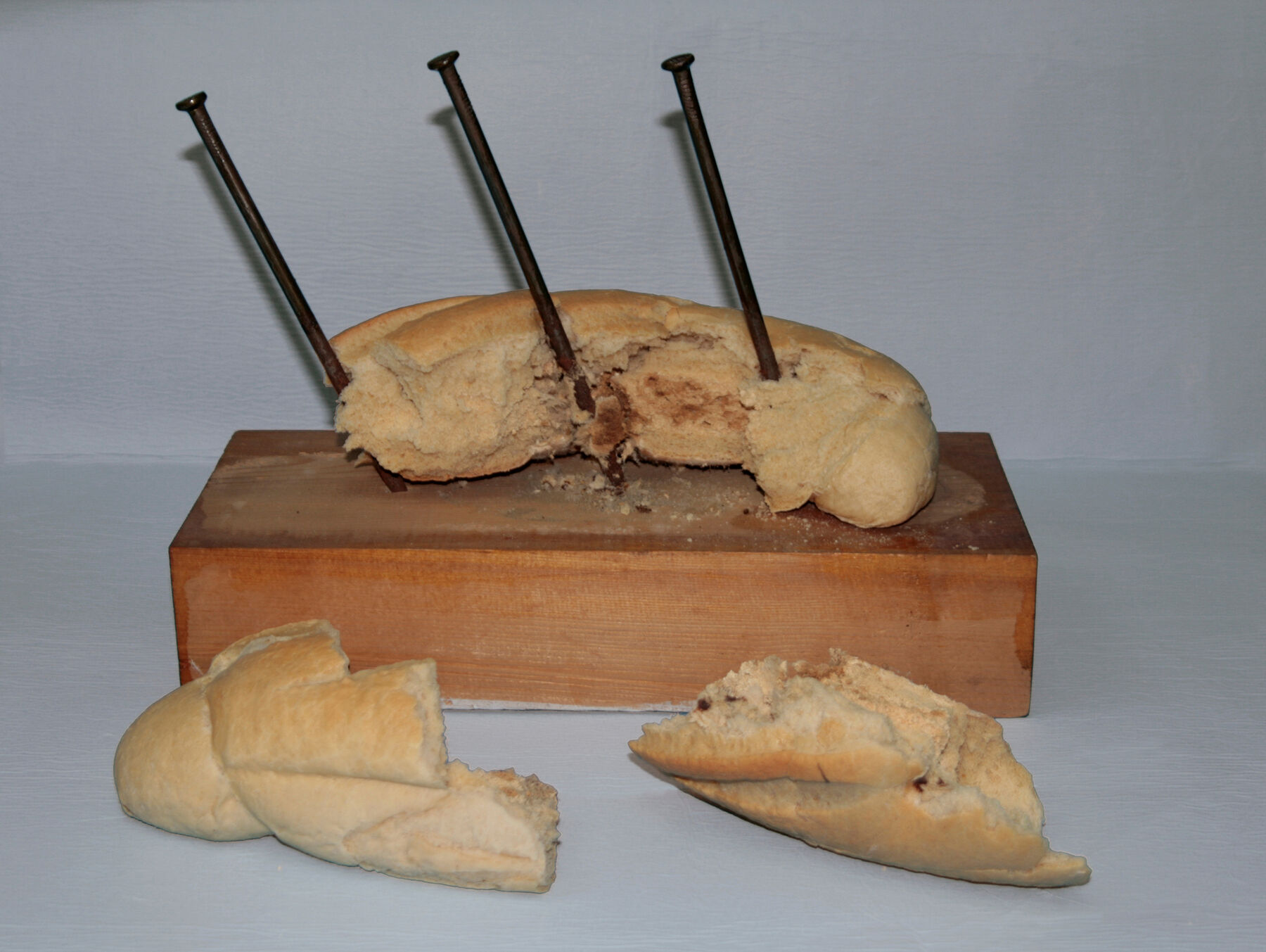 Crumbling bread on slab with nails drilled in; two removed bread chunks in front of slab