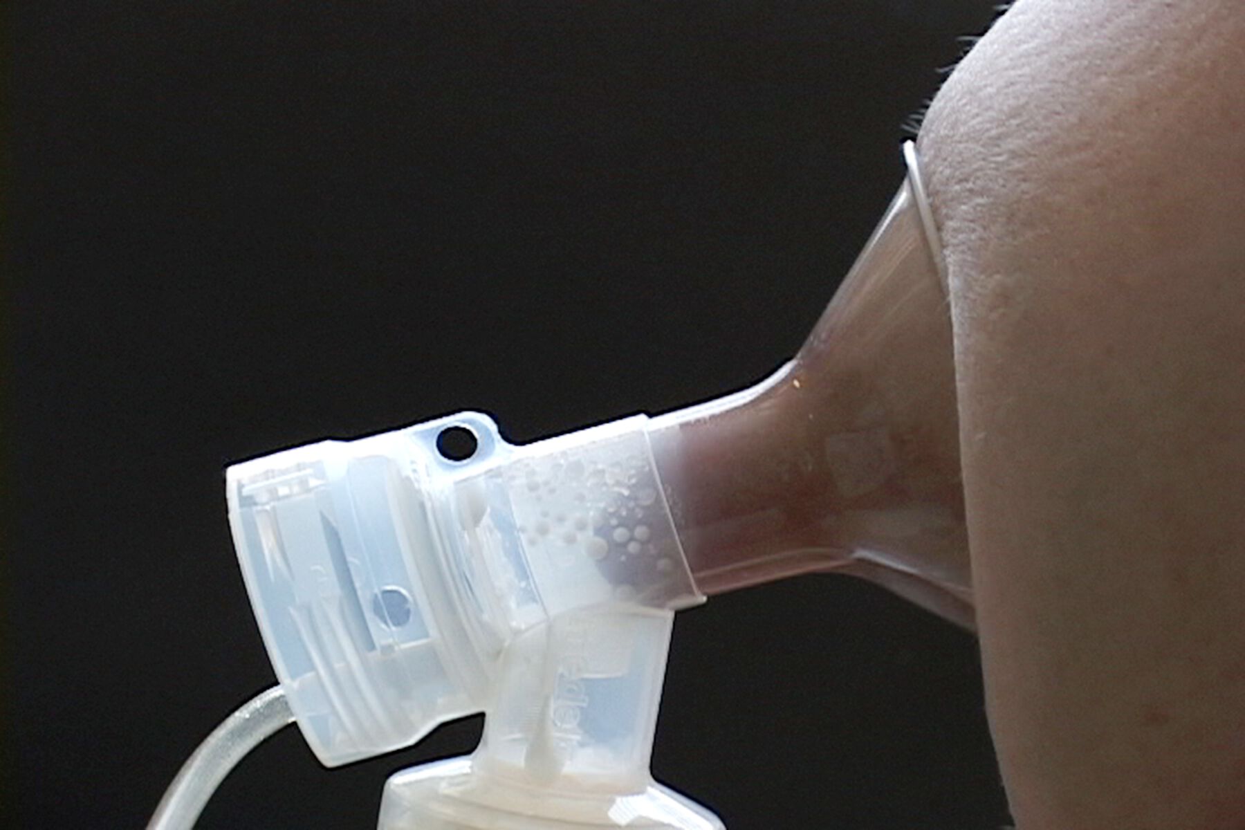 Side closeup of breast with nipple in suction cup with tube and bottle to collect milk