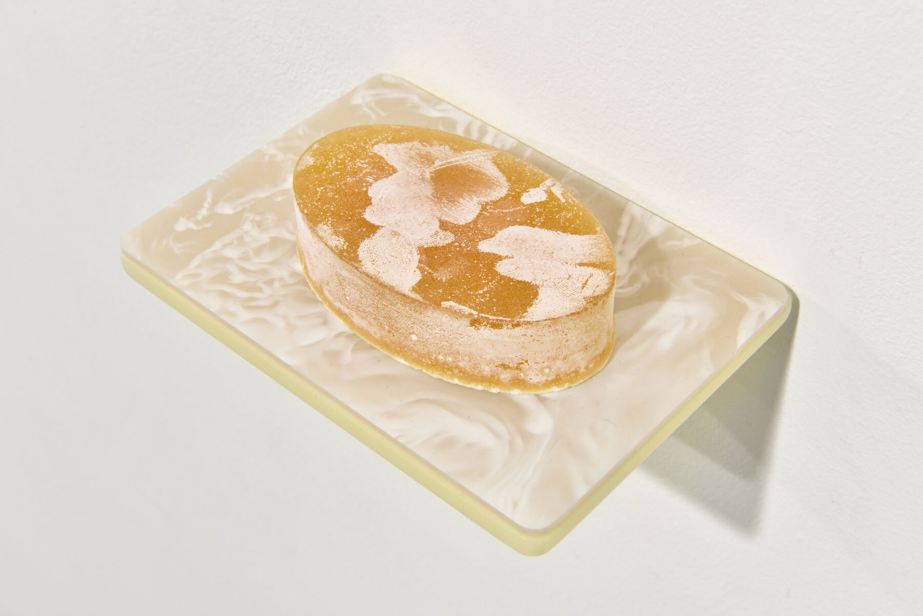 Overhead closeup of golden-yellow soap with white chalky patterning on marble-patterned dish attached to wall