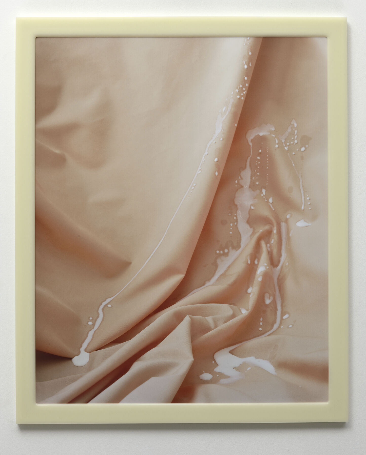 Print of white liquid droplets carving path down pinkish-peach cloth with crinkles (inside cream frame)
