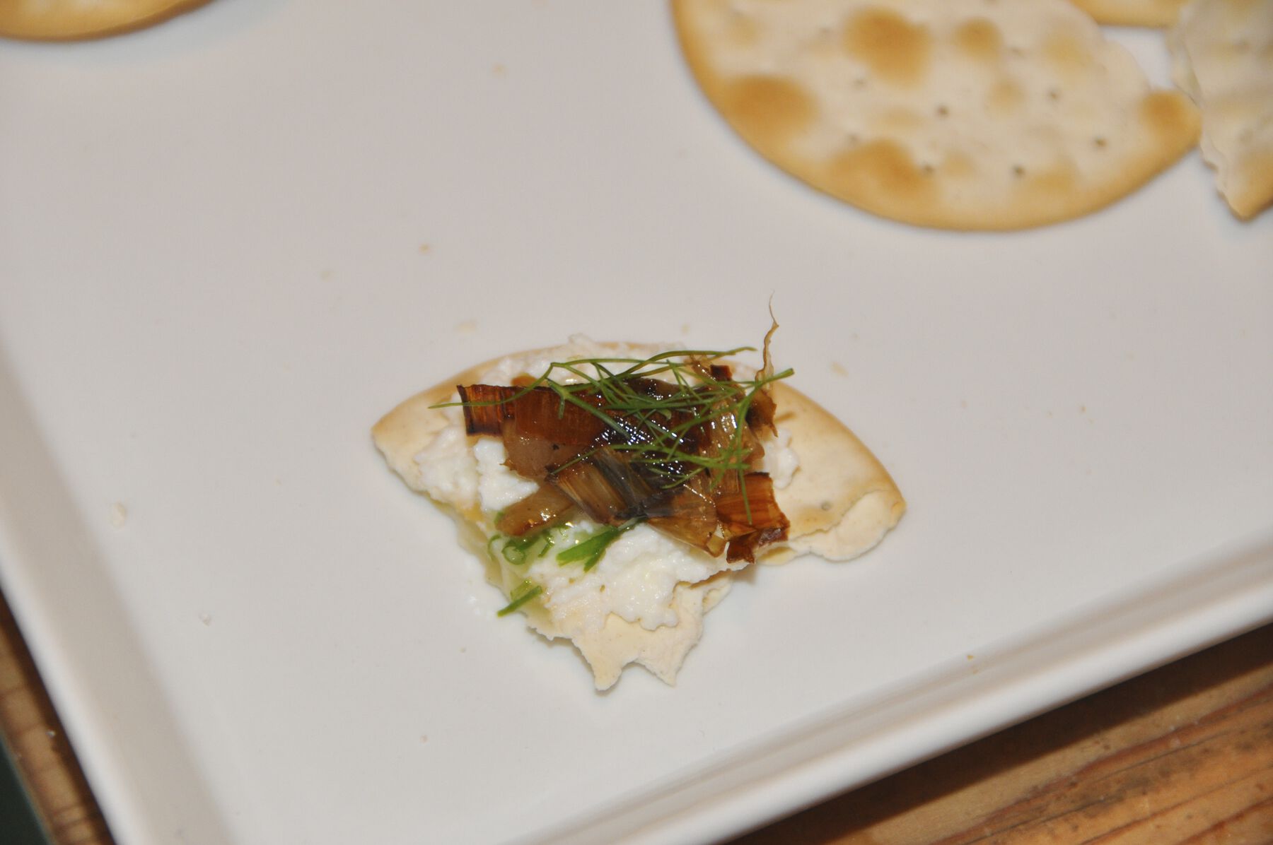 Red and green seasoning and white cream placed upon broken-off section of cracker in white tray