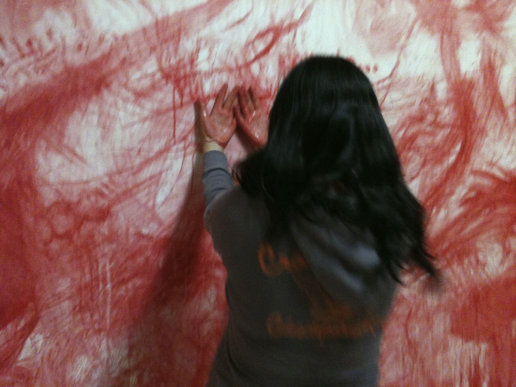 Visitor with reddened palms placing backs of hands to blurred, smudged red strokes on wall