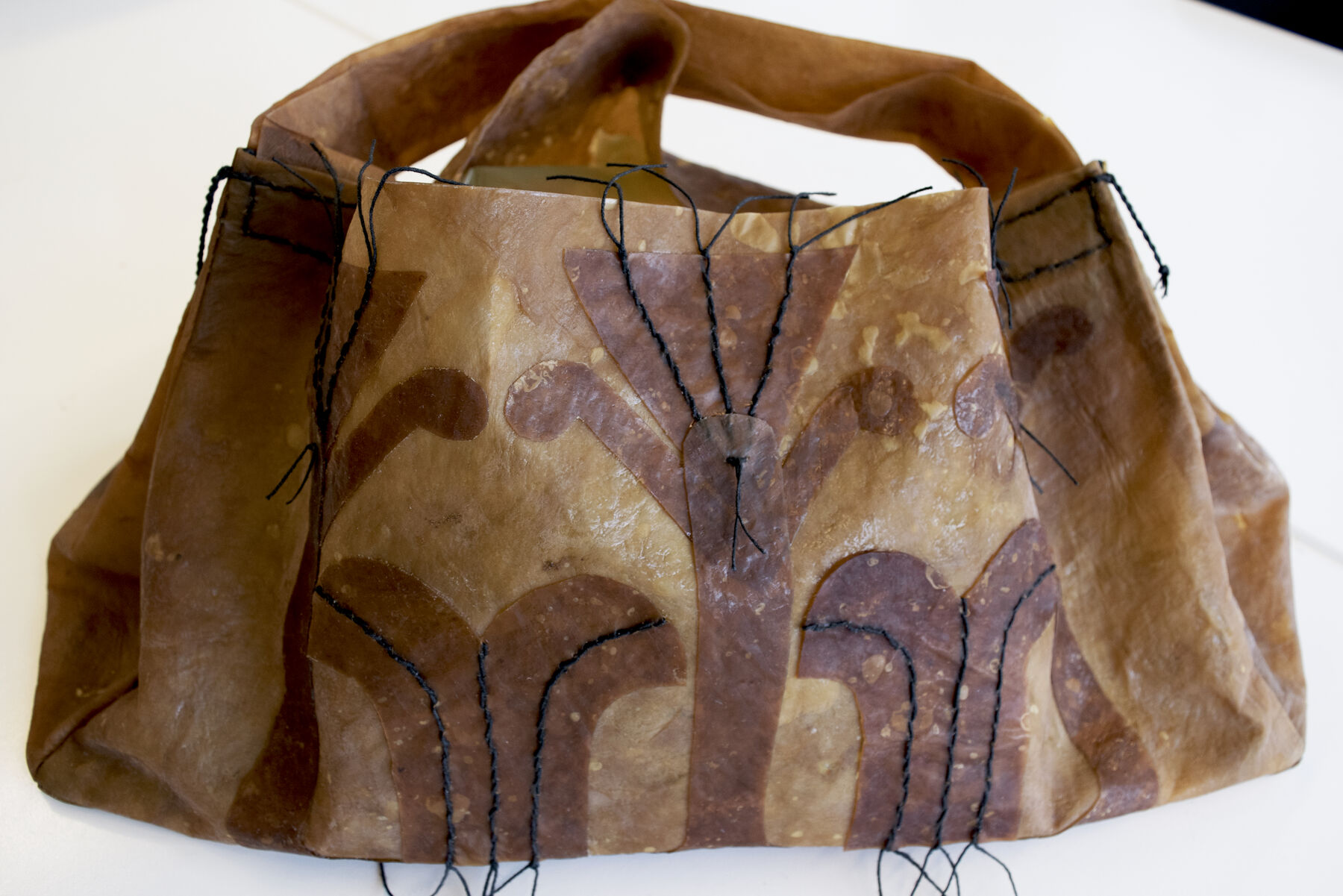 Dry, stiff papery tan bag with brown patterns and black embroidered lines and sowed handle