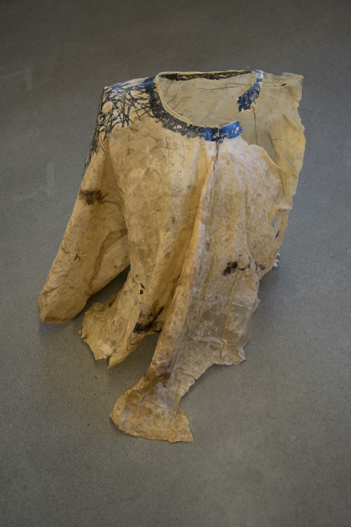 Tan stiff paper-like fabric with circular rim and torn, fragmented folds emerging; has black printed geometric designs