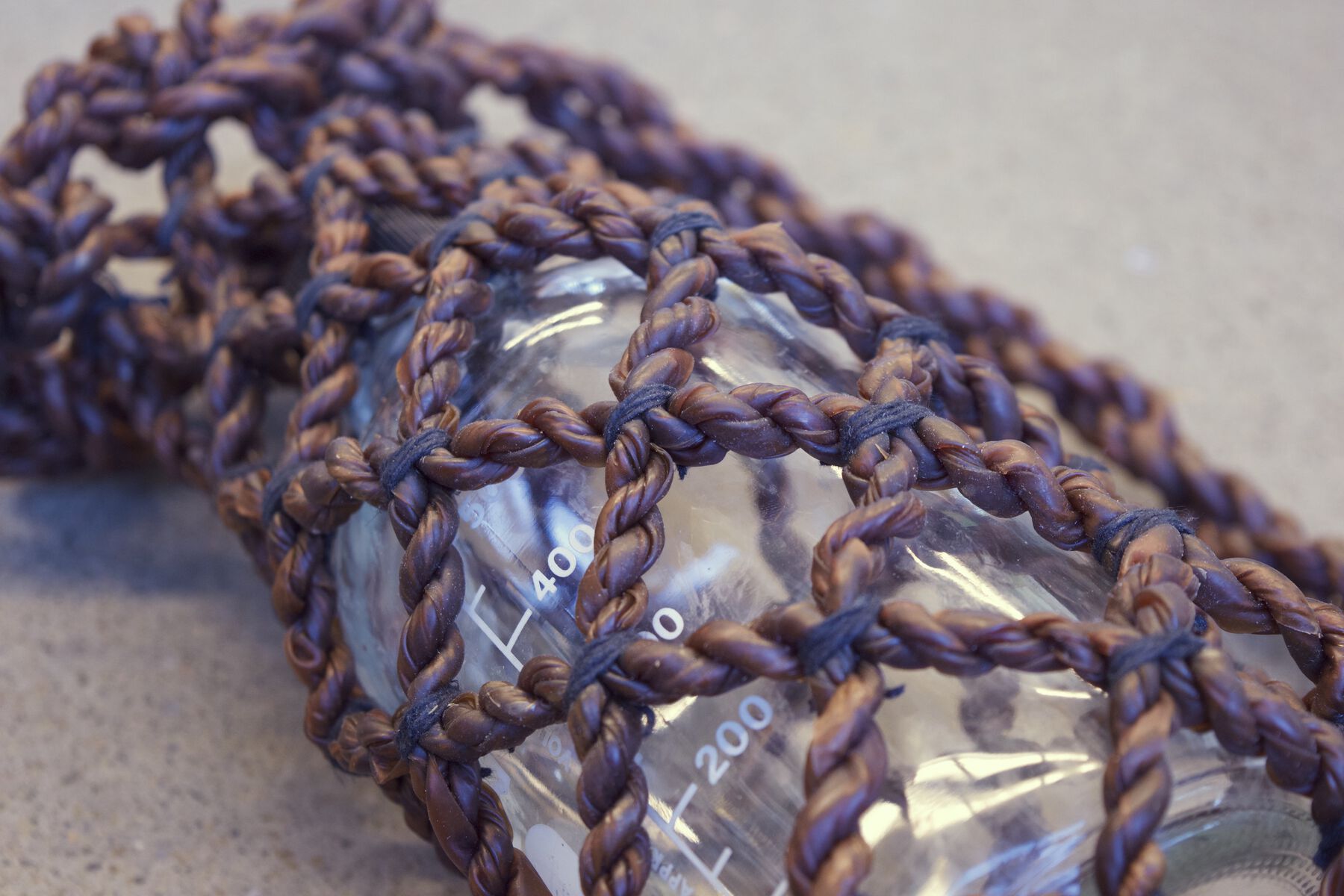 Mauve braided rope in diamond lattice bag holding transparent (plastic) container with measuring lines