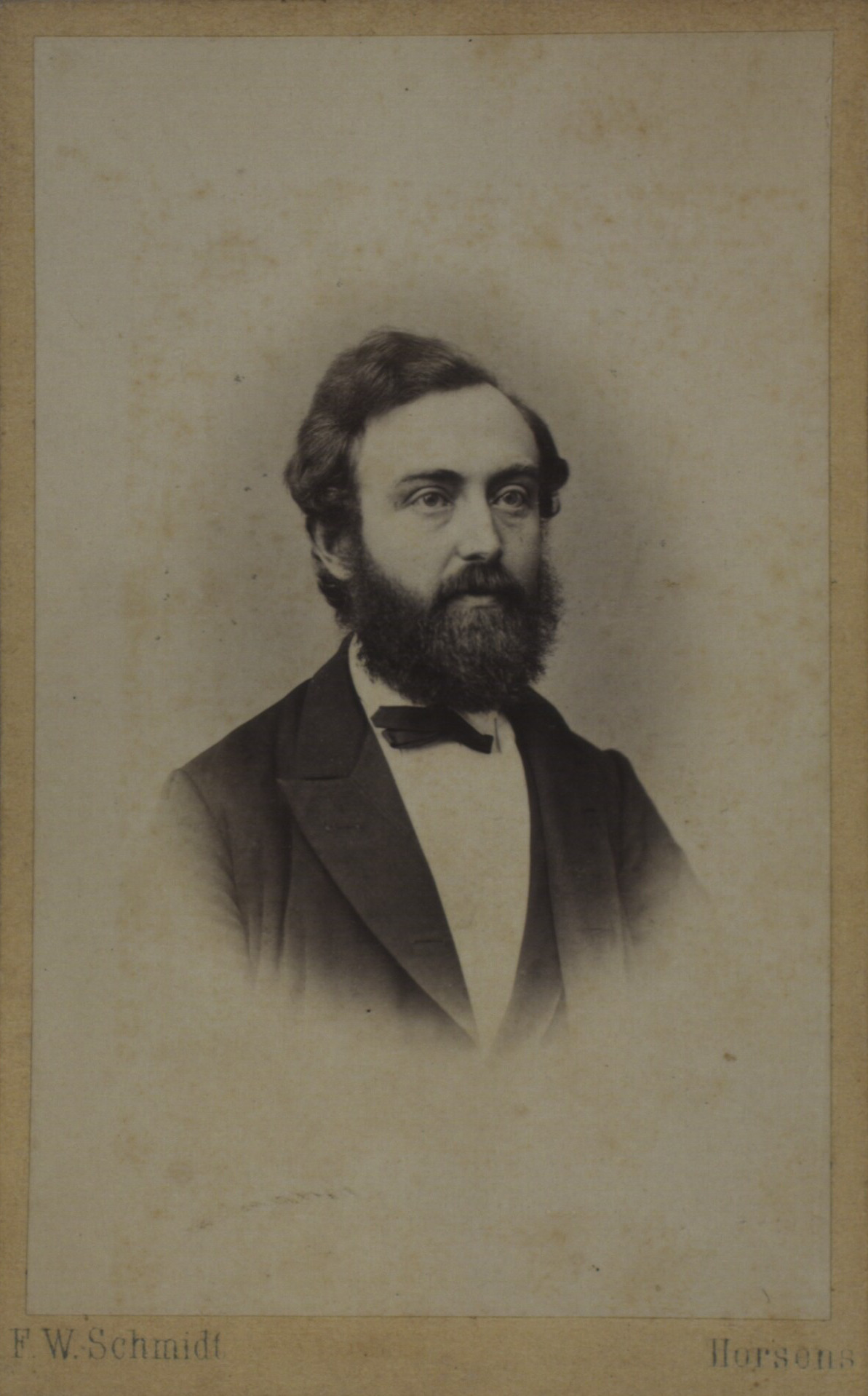 Portrait of a man in black and white. He has short hair and a full beard, and he wears a tuxedo with a bowtie. Only a portion of the upper half of his body is visible. 