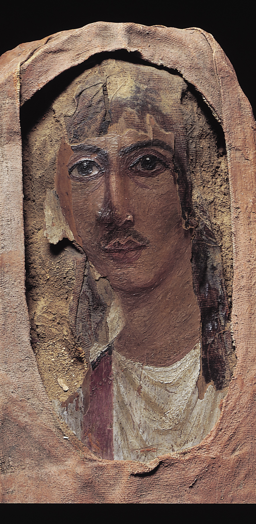 Portrait of a man attached to a mummified individual as indicated by the linen wrappings that can be seen around the painting. There are substantial paint losses to the top, right, and left edges of the portrait. The depicted man has dark eyes and eyebrows and a thin moustache. He wears a white tunic with a wide reddish-brown vertical stripe coming down each shoulder.
