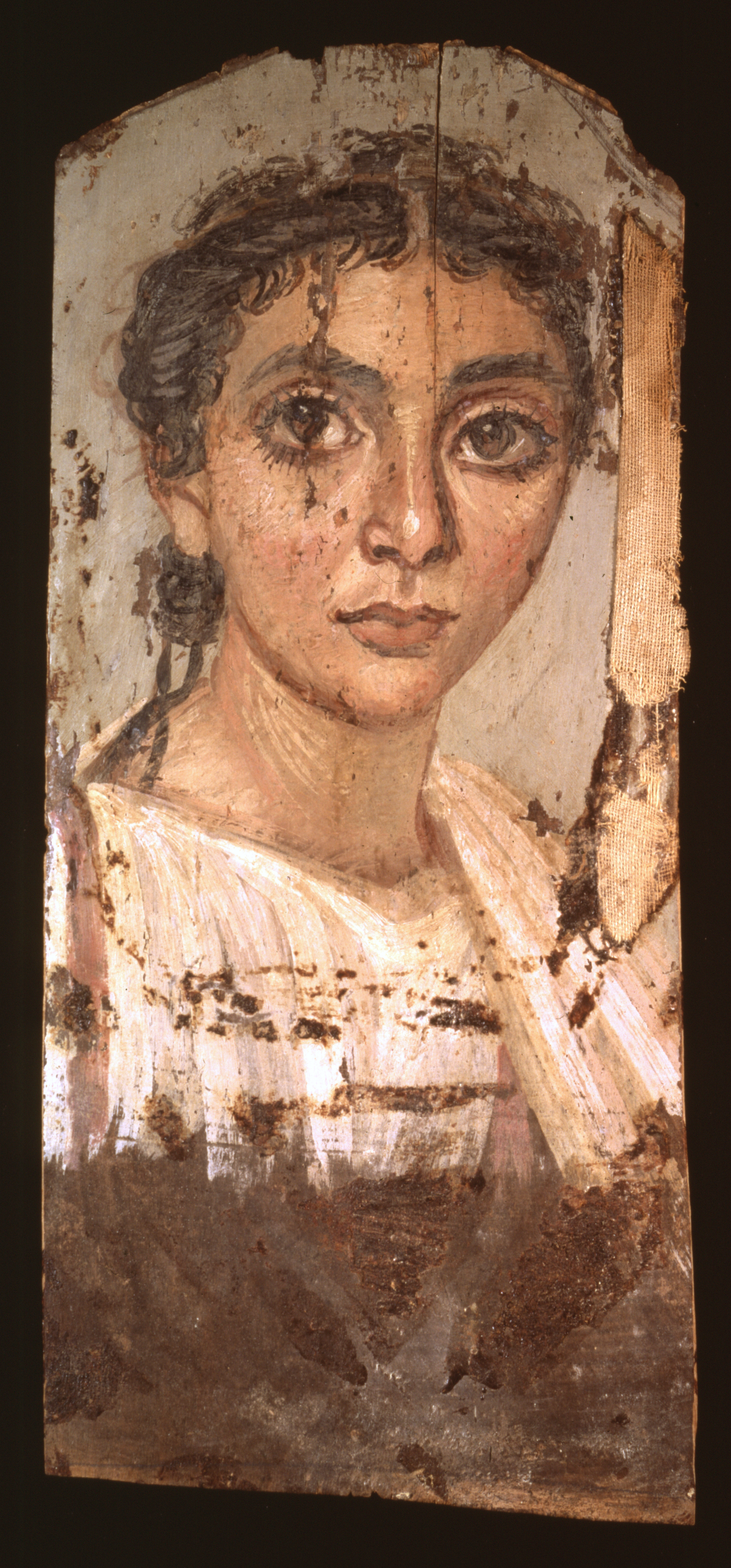 Portrait of a woman with a rounded face, curly hair that is pulled back and tied in a low a bun, prominent dark eyebrows, big brown eyes, a long nose, and a small mouth. She wears a white tunic. There are some paint losses to the right edge of the painting, and the lower section of the portrait, below the woman's chest, is unpainted.