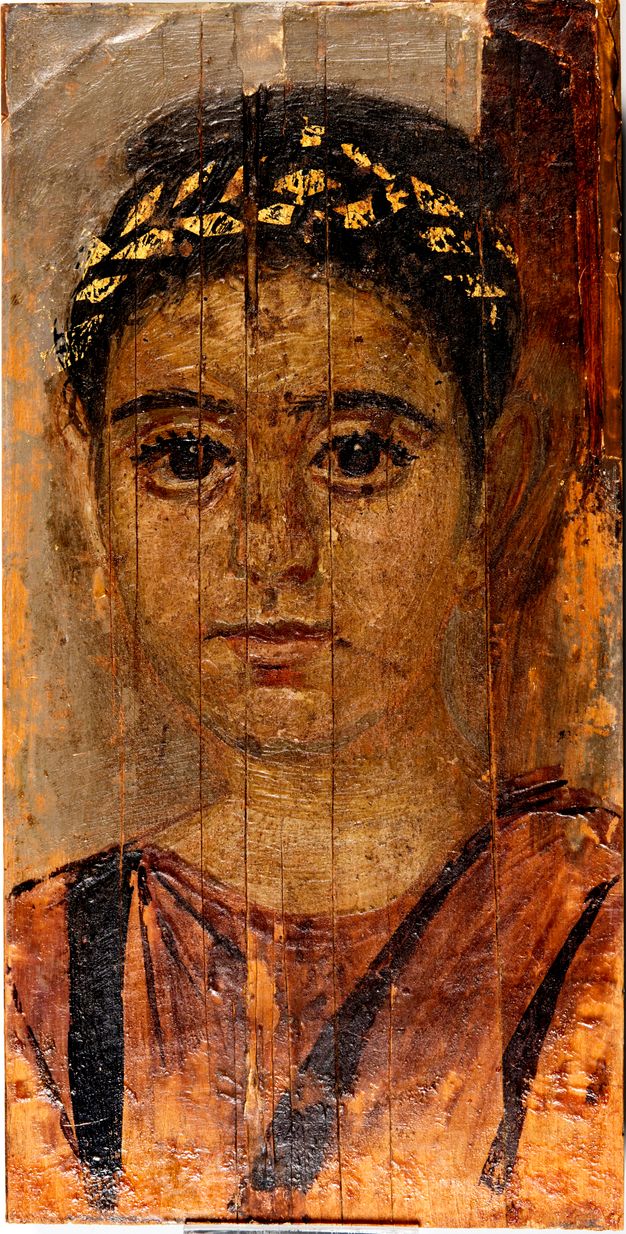 Portrait of a young girl in a red tunic with a gold wreath decorating her dark hair, which is styled in an updo. She is also wearing small gold earrings. There is a brown cast over the image. There are vertical cracks in the material.
