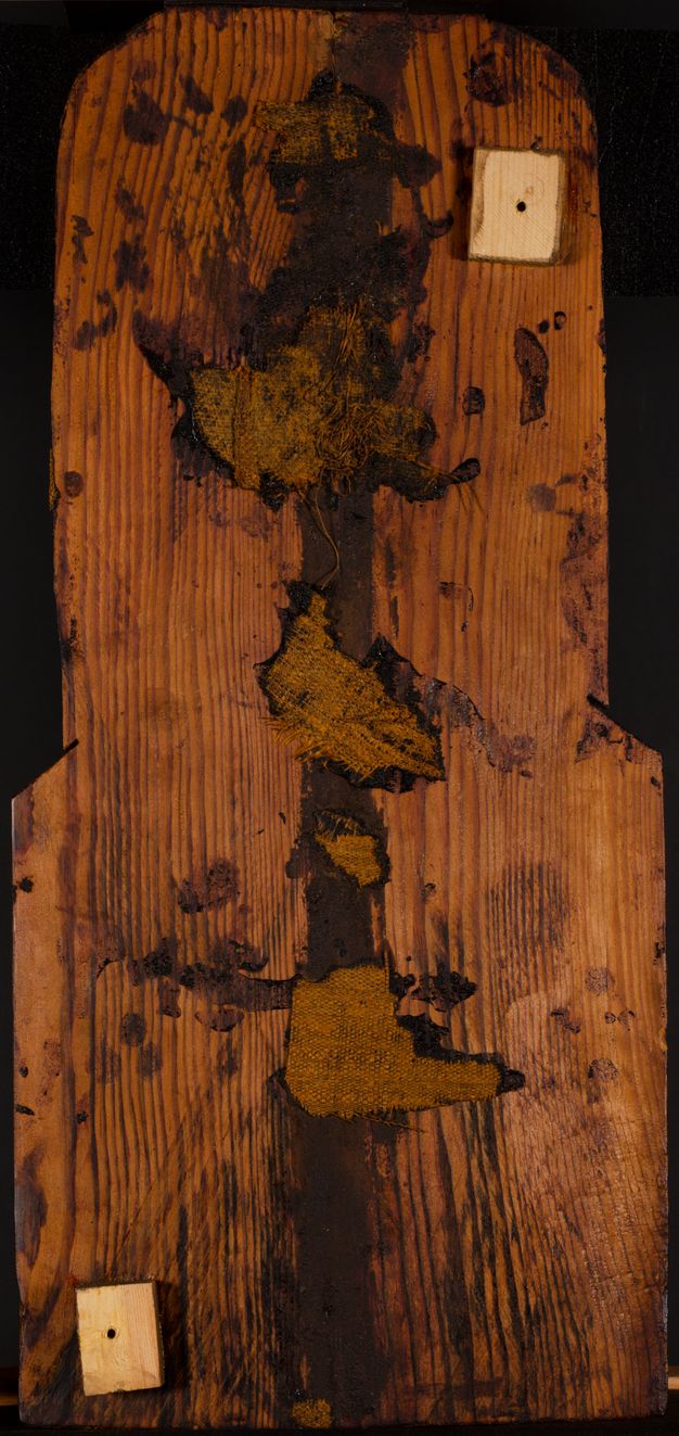 Image of the back of the panel. In the upper right corner is a newer square piece of wood that is paler than the panel and has a hole in the center. A similar piece of wood appears in the bottom left corner. Down the center of the panel is a dark stain with patches of fabric applied along the break.