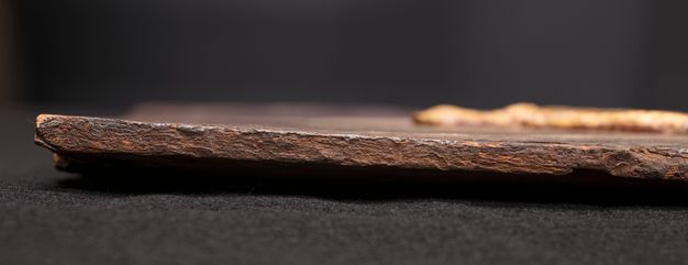 Edge of a painting lying flat on a surface showing an overlapping paint layer. There is a raised layer of paint out of focus towards the right edge of the image.