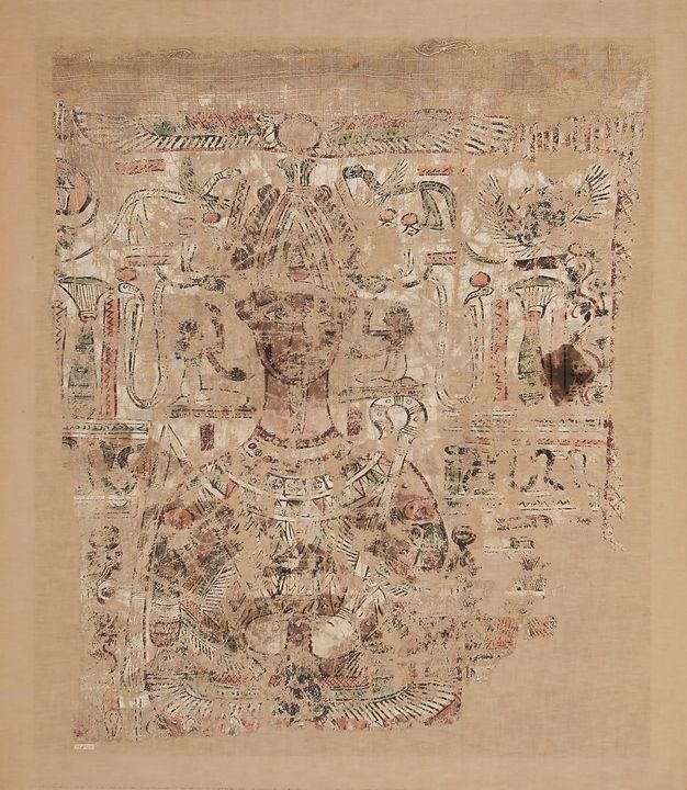 Photo of the Osiris shroud in color. The shroud has remnants of tasseled fringe at the top edge and is painted in red, orange, yellow, green, red-pink, and black on a white ground. Only the upper half of the shroud remains. Osiris wears a false beard and atef crown and wields a crook and flail. He is adorned with a colorful geometric pectoral and a large necklace with a naos pendant. There are two tall lotus bouquets on either side of him, hieroglyphs, mythological creatures like sacred winged serpents, uraei, and a winged sun disk, and architectural and vegetal elements. There are considerable losses to the textile and paint layers, so the image is fragmented. A dark-brown stain appears on the proper left side of the shroud.