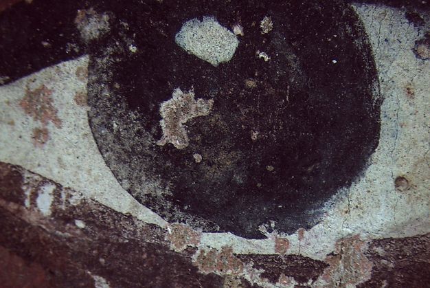 Visible image of the proper left eye in Figure 5.1. The eye is dark and without a pupil. A dot of white at the top gives the impression of the reflection of light. The paint shows wear.