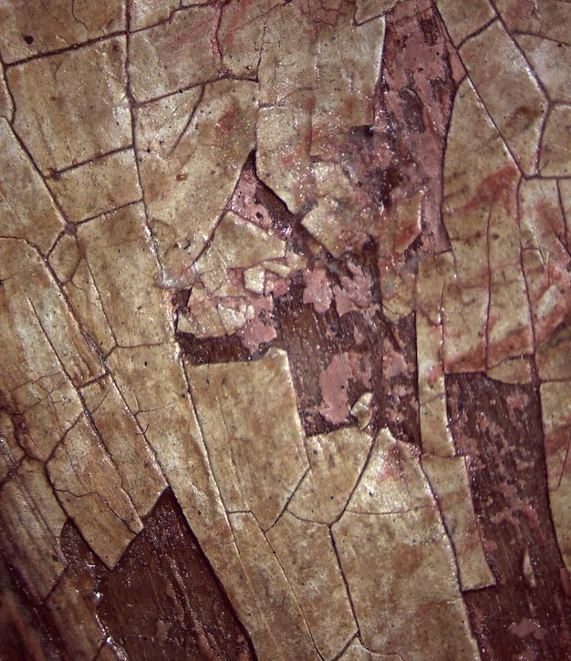 Microscopic detail of an area on the forehead on figure 5.2 showing cracks on the paint surface, which features pink and tan colors over a brown ground.