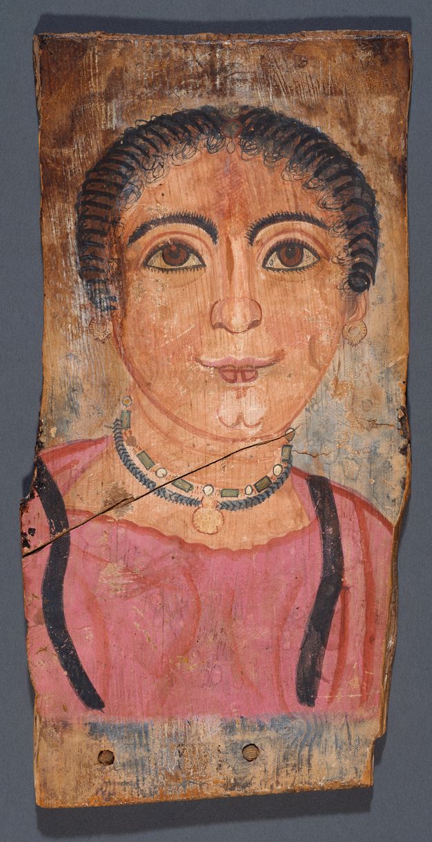 Portrait of a woman with dark brown textured hair that is pulled back. Her eyes are brown, and her skin is fair and pink. She has a pink tint to her cheeks, forehead, and lips. The woman is wearing round earrings and two blue necklaces. One of the two necklaces is beaded with round white beads and rectangle blue beads. The other necklace has a small chevron pattern and is blue with a circular pendant. The woman is wearing a pink garment, with black detailing on each side of her chest. The background of the portrait is primarily brown.  