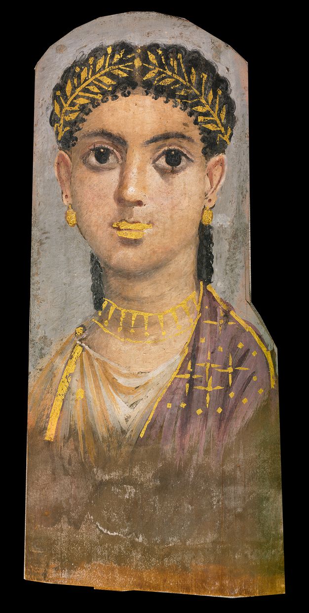 Portrait of a girl with dark hair and dark eyes. Her skin is fair and pale, with a pink tint on her nose and ears. She is wearing a gold wreath around her head, as well as gold round earrings and a gold layered necklace. She appears to be wearing gold lipstick. She is wearing a purple and white garment with gold star-like detailing on the right side and gold ribbon-like vertical detailing on the left side. The background is grey.