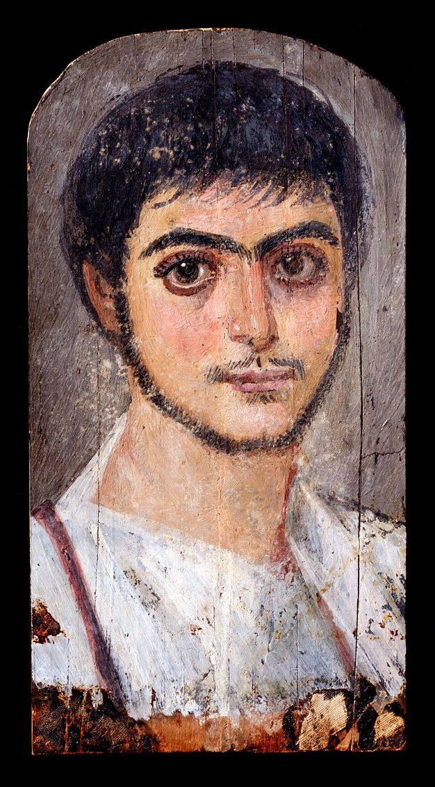 Portrait of a bearded man wearing a white tunic. His beard shadows his jaw with a thin mustache on his upper lip. 