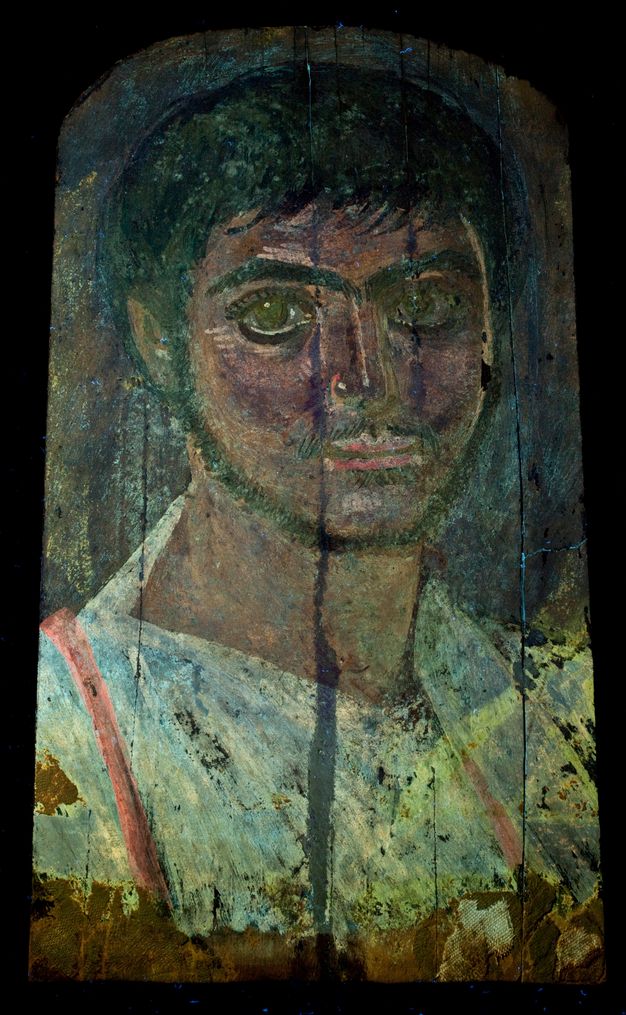 Ultraviolet-induced visible fluorescence image of a portrait. The paint used for skin takes on a dark brown shade, and the white in the tunic looks blue. There is a vertical stripe of red across each shoulder.