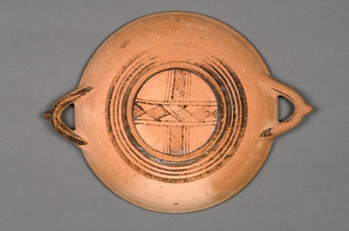 Bottom of a red terracotta plate decorated with now-faded black bands around the foot. Within the foot are two intersecting patterned bands made up of diamond-shaped hatching. The plate has two handles, one on each side, and the number 2801 is written in pencil halfway up the body.
