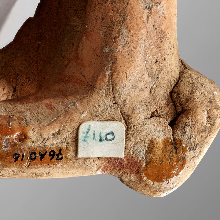 The underside of the ape statuette showing a number written in black. A white price label with the pound symbol and the number 110 in green ink is affixed near the written number quote 76.AD.16 end quote.