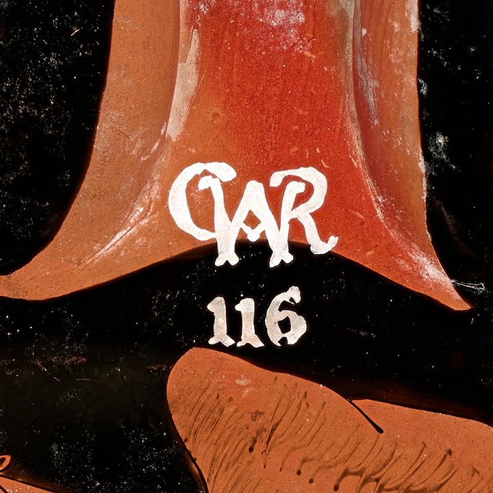 White label with a ligature and a number painted in white against a black and red background. The letter W has a letter C hooked around the left leg, as the right leg creates the backbone of a letter R. The upside-down V made in the W is turned into an A with the addition of a crossbar. The number 116 is immediately below.
