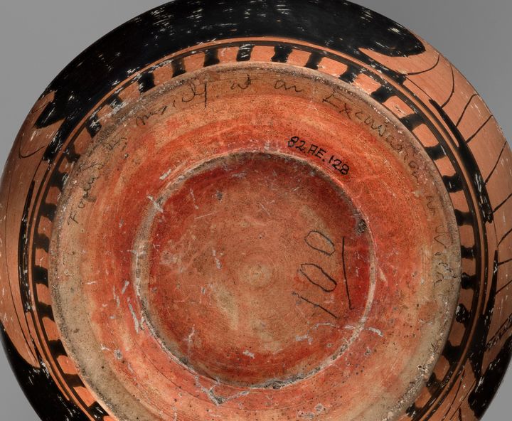 Underside of a ceramic vessel with three written inscriptions. Following the curve of the vessel’s foot is text in pencil that reads quote Found by myself at an excavation at Nola end quote. Also in pencil and closer to the center is the number 100, which is underlined. Between the two inscriptions is inked text reading quote 82 AE.128 end quote.
