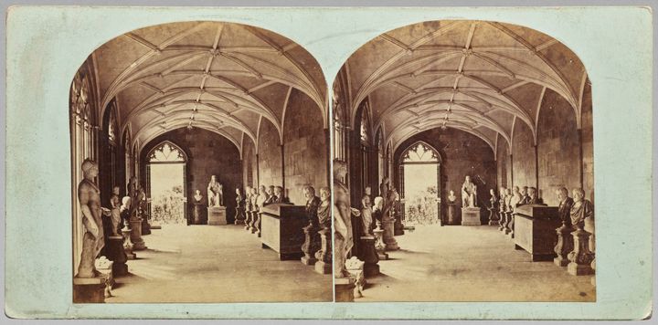 Stereoscopic view of a long corridor with a ribbed, vaulted ceiling lined with busts and full-body sculptures. It includes two arched, sepia-toned photographs of the same hallway from slightly different angles.