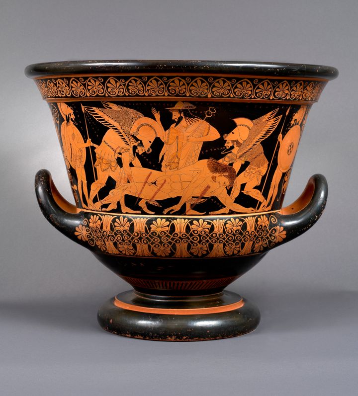 Terracotta krater with a short foot, tall sides that flare widely, and two upward curving handles. The surface of the vessel is decorated with outlines of a scene on a black background. Three men stand around a prone, naked man, who bleeds from wounds in his chest, abdomen, and upper thigh. He is being supported by two winged, bearded figures with helmets on their heads.