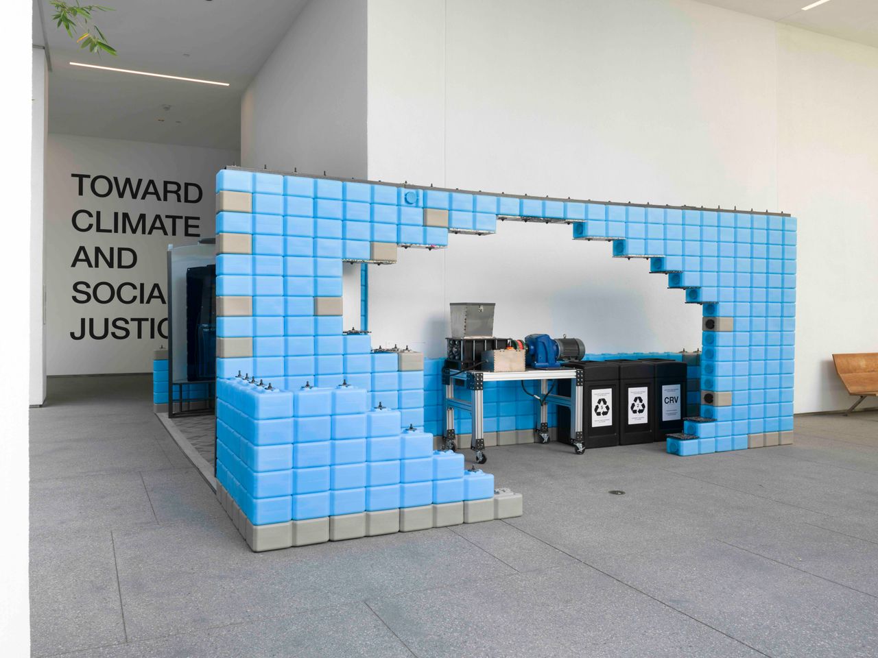 Modular light blue block installation with recycling bins and equipment with quote Toward Climate and Social Justice end quote written on a white wall behind it.