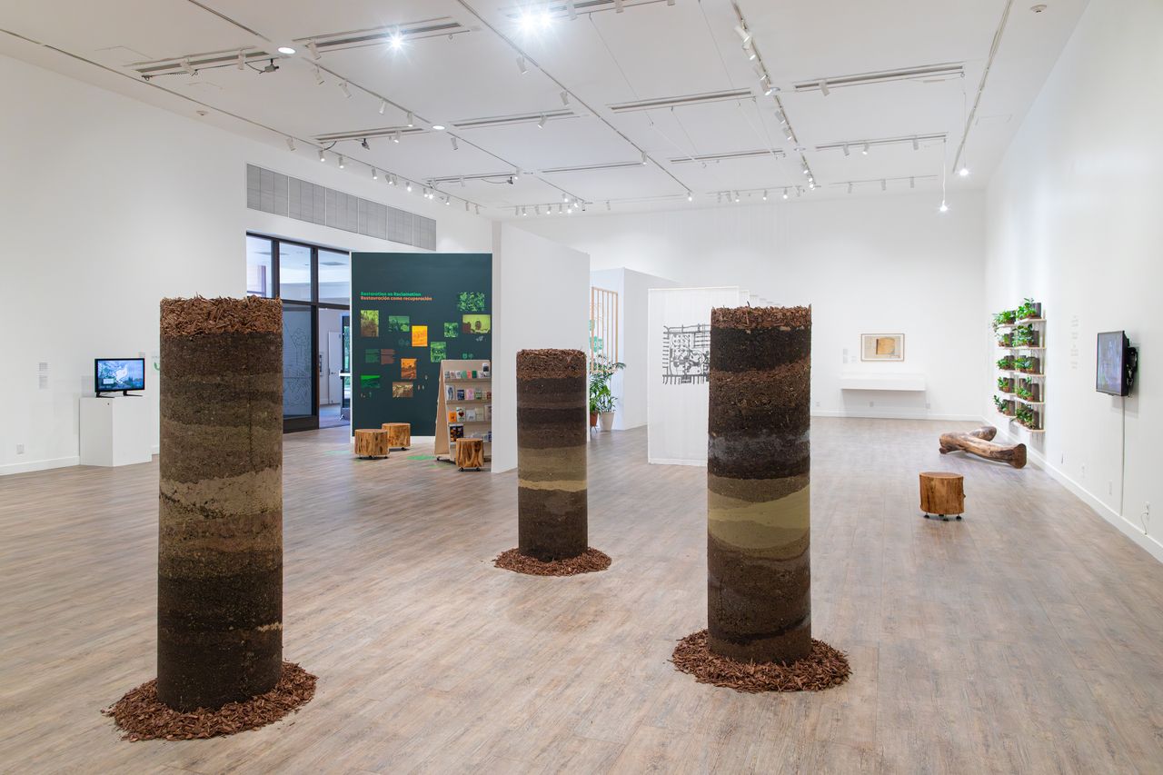 Indoor gallery space featuring tall circular stacks of soil and rocks of varied colors.