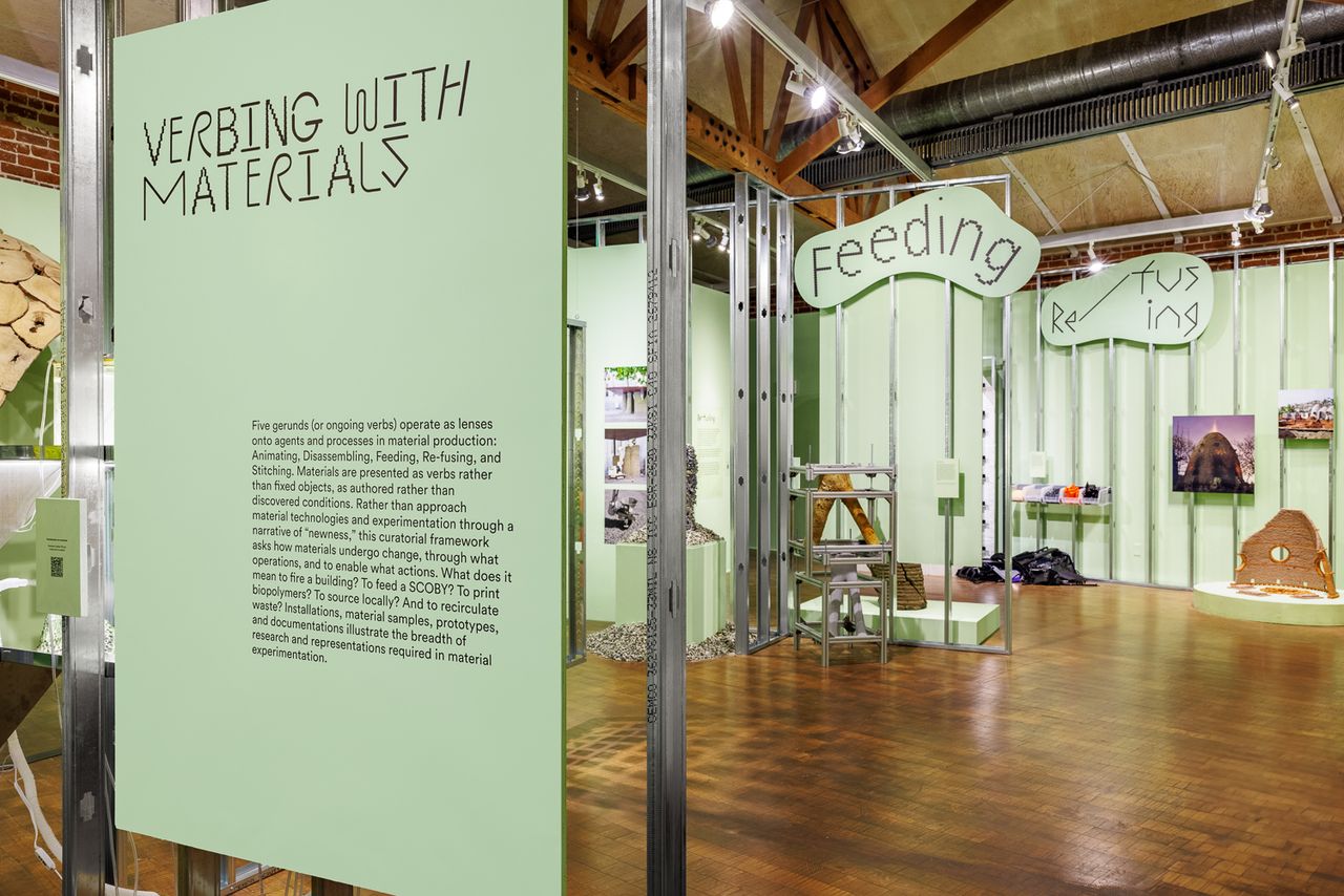 Green sign that says quote Material Acts end quote against a green wall with cardboard and storage boxes to the sides.