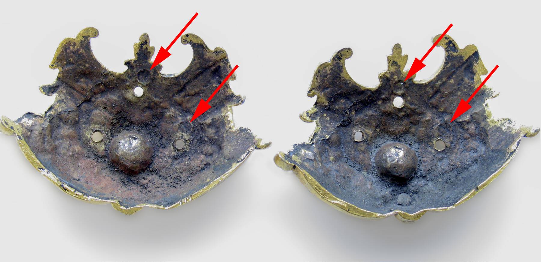photograph of the reverse of two corner mounts; red arrows are superimposed onto the image and point to old screw holes