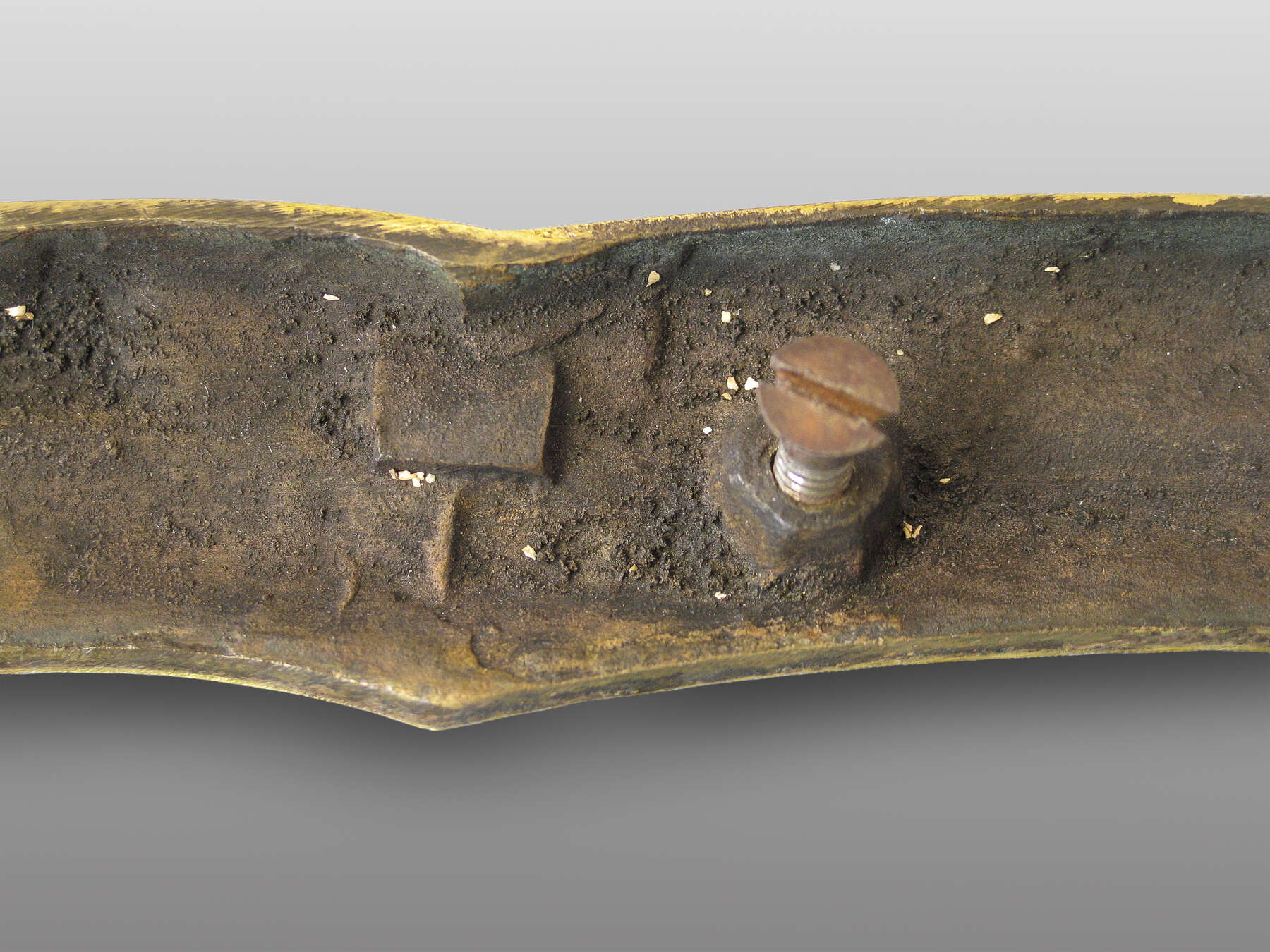 the weathered back of a gilt bronze mount with a threaded bolt protruding from a nut