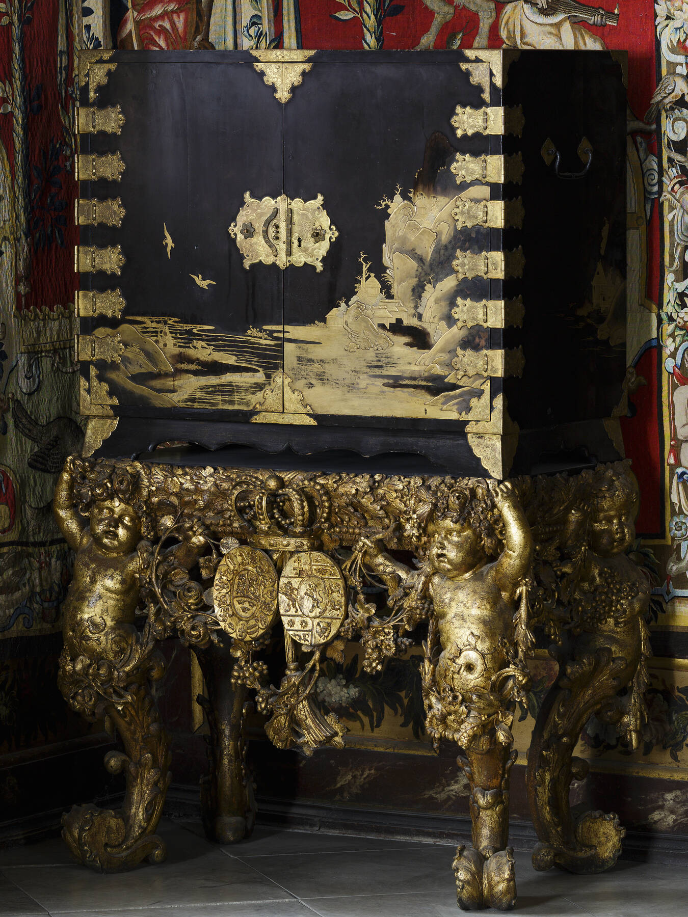 a three-quarter view of an incredibly elaborate Japanese cabinet, featuring a gold lacquer landscape scene with rocky outcroppings, flying birds, pagodas, and a body of water