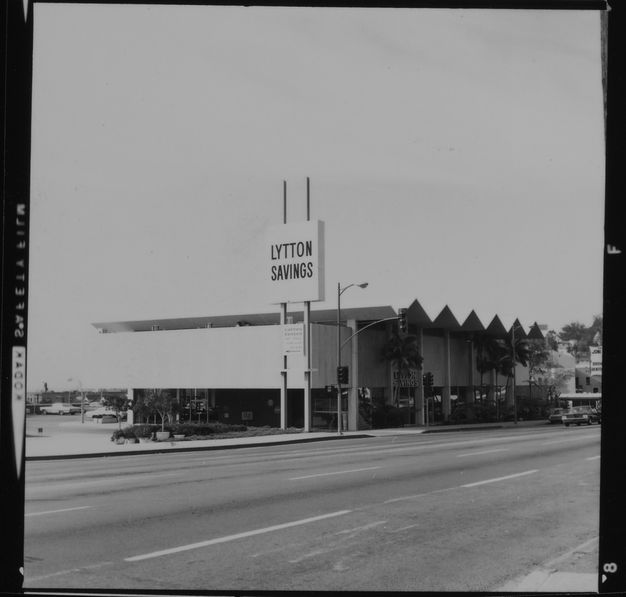 A black-and-white photo featuring a bank building shown from across the street. A sign reading “Lytton Savings” appears in front of the building.