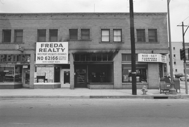 A black-and-white photo features a two-story commercial building shot from across the street. A sign near the center reads “Freda Realty.”