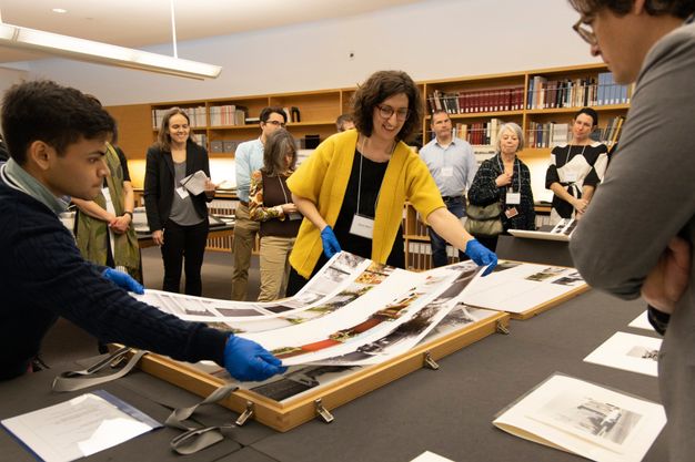 A group of people stand around a table displaying photos and archival material in the Getty Research Institute’s special collections seminar room.