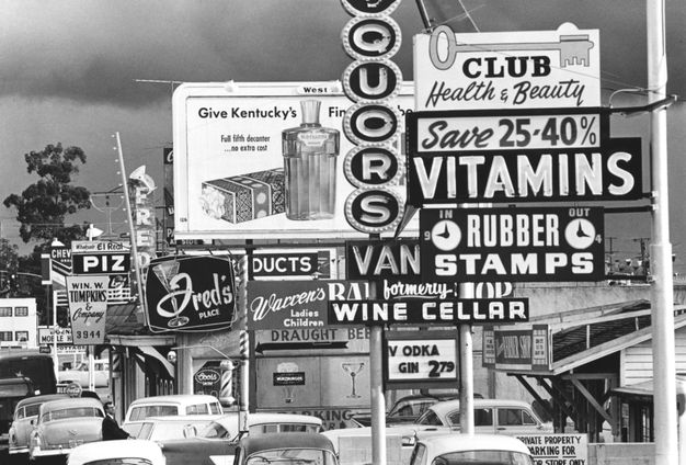 A sepia photo features a city street filled with billboards and store signs.