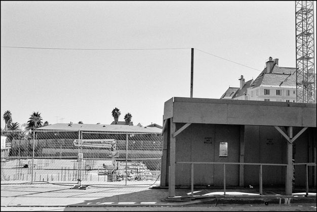 A black-and-white photo features a street scene of a construction site and a temporary walkway at right. At left is a chain link fence.