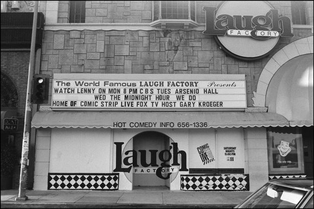 A black-and-white photograph of a building facade with a prominent marquee displaying the words “The World Famous LAUGH FACTORY.” The marquee advertises various comedy shows and provides contact information.