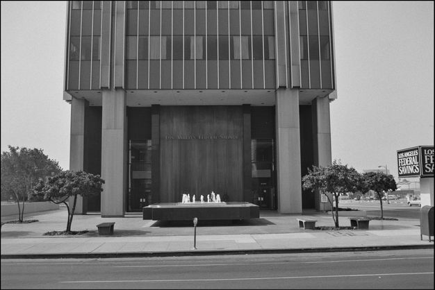 A black-and-white photograph of a large building with a small fountain in front of it. It has the words “Los Angeles Federal Savings” on the front, and there is a street and parking meter in the foreground.