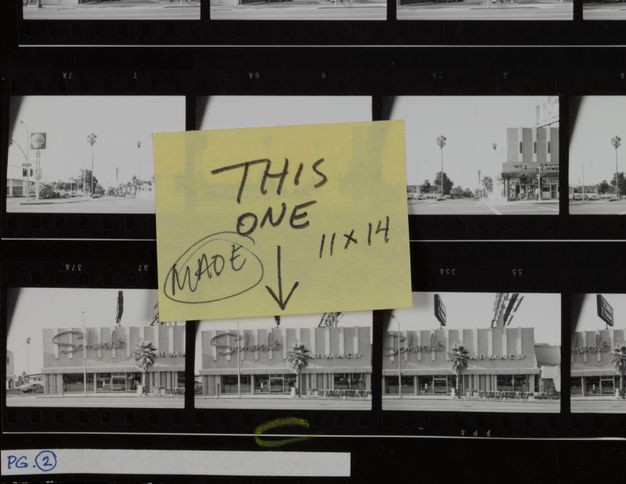 A contact sheet shows six black-and-white photos of store façades shot from the street. Affixed atop one of the photos, and blocking the photo above it, is a yellow sticky note that reads “this one, made, 11 x 14.”