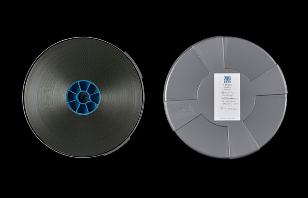 A color photo featuring two film reels shown, one placed above the other. One is gray and one is black.