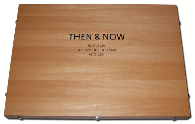 A hard-cover book is shown with its light brown case cracked open at a small angle, revealing a white paper beneath. The encasement reads “Then & Now.”