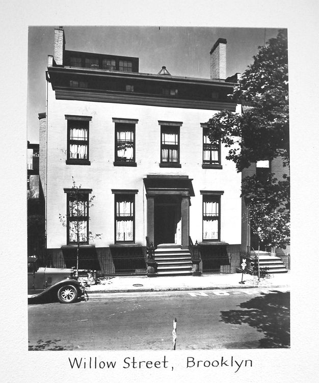 A black-and-white photo of a two-story white house and a road in front of it.