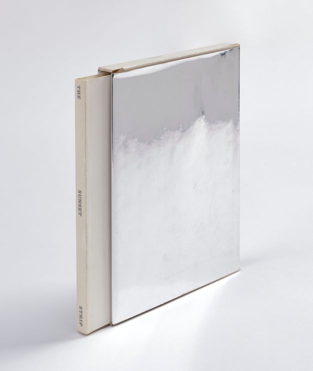 A silver covered book is shown at a high angle, sliding out from its silver encasement.