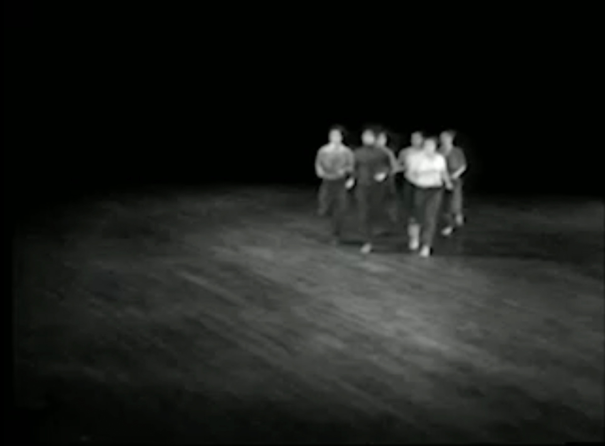 Black-and-white video of view from above stage left showing an empty stage and dancers moving across it intermittently.